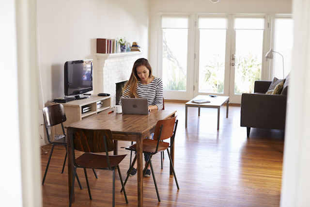 Woman Working From Home Using Laptop On Dining Table